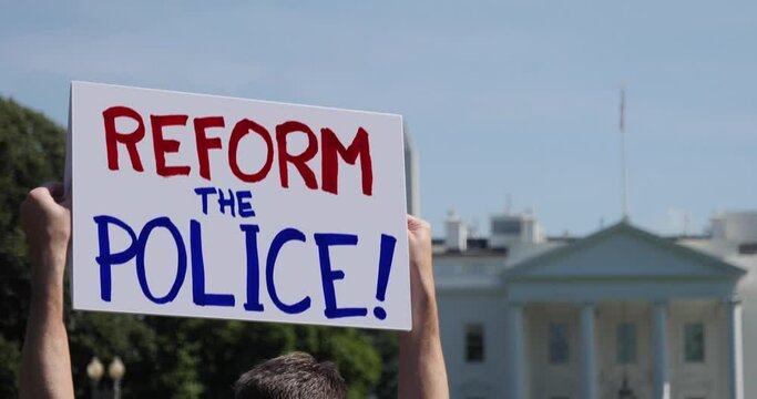 A man waves a handmade REFORM THE POLICE protest sign outside the White House.
