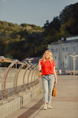 Beautiful girl walk in the summer Kiev City. Young woman tourist on a street. Street style portrait. Stylish girl near a river weared in red casual outfit. Life style. Local tourism. Srteet walk. 