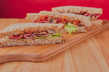 Bacon,lettuce,tomato and mushroom sandwiches,resting on wooden chopping board. 
