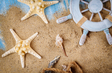 Sandy beach in old blue wood background on decorative steering wheel with starfish, seashells