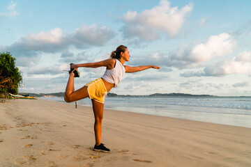 Fit young woman in bright sports outfit stretching legs on the beach during outdoor work out....