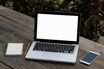 Laptop computer with white blank screen monitor with mobile and notebook on old wooden table with blurred background