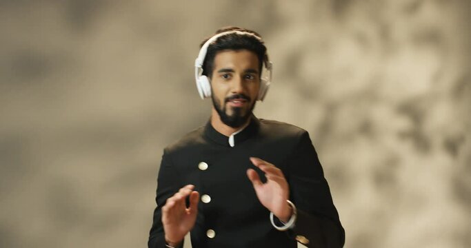 Hindu young handsome man with beard dancing cheerfully in headphones while listening to music. Indian male dance and having fun. Guy moving in rhythm with favorite song.