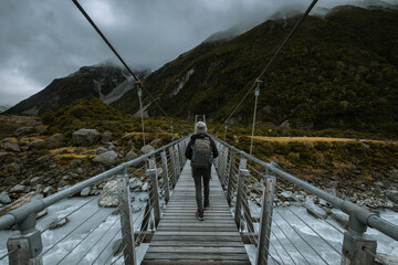 back shot of young woman tourist with backpack walking on suspension bridge over the river in...