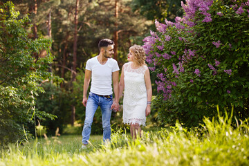 Young man and woman couple near a blooming lilac bush. Tender holding each other. Spring lovestory. Blonde-haired girl with curled hairs and man weared in casual. Young family