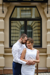 Fototapeta premium Young Bride and Groom couple in summer City. Tender holding each other. Woman and man couple.Romantic date of young happy family on window background. Gender traditional newlyweds street style wedding