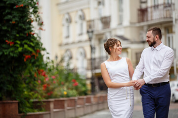 Fototapeta premium Young Bride and Groom couple in summer old City garden. Tender holding each other. woman and man couple. Romantic walk of young happy family near hydrangea bush. lovers newlyweds street style wedding