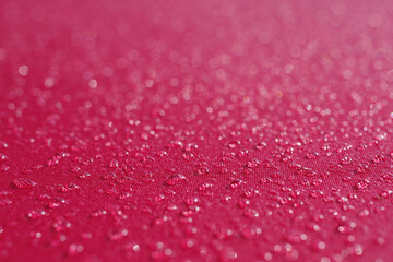 Close-up full frame macro view with selected focus on water drops from morning fog on the red fabric of an umbrella