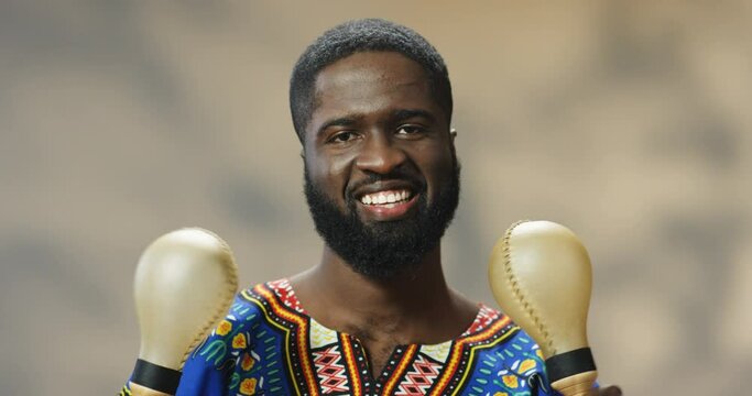 Portrait of handsome young African American man smiling cheerfully and playing on maracas. Close up of happy guy holding musical instruments and making rhytm to music while shaking.