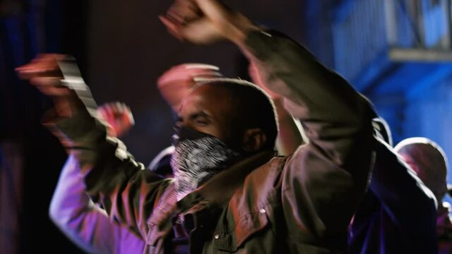Mixed-races young men rebels with masked faces screaming mottos and shouting slogans at night in smoke at rebellion. Multiethnic males at riot against police violence and for black lives matter.