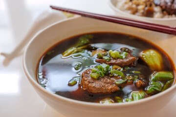 Selected focus view at Taiwanese stew Beef Noodle Soup without noodle in white bowl on white table.