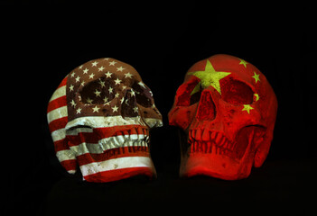 Two skulls with Chinese and American national flag or emblem projected over the surface isolated against a plain black background.