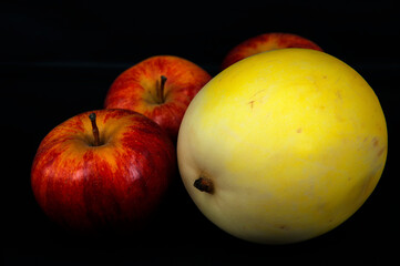 art photo ripe yellow melon with red apples on a black background
