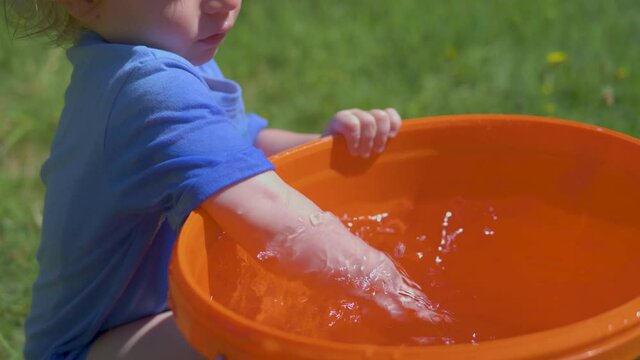 Toddler joyfully plays and splashes water from a bucket on a hot, bright summer day