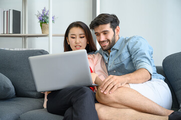 Fototapeta premium Happy and relax lifestyle of young couple lover wearing casual dress together working on sofa with laptop notebook computer in living room at home.