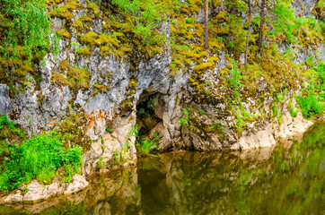 Cave in a rock near a mountain river in summer.