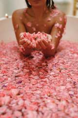 Woman enjoying smell of flowers petals in her hands in round outdoor bath with tropical flowers, organic skin care, luxury spa hotel, lifestyle photo