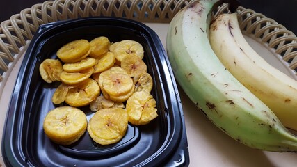 A plate of fried Plantain chips and two raw plantains on a tray