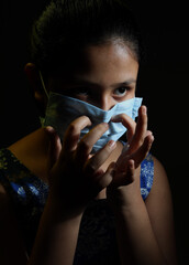 Close up of an Asian girl wearing medical protective mask to health protection and prevention against coronavirus or covi-19, flue, epidemic and infectious diseases posing in the darkness, text space,