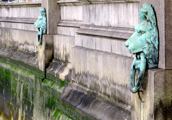 covered in green patina lion heads with rings in their teeth on the waterfront Thames in London