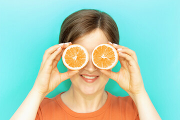 The girl in front of her eyes holds slices of oranges, on blue background