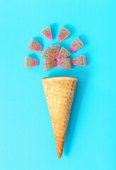Ice cream waffle cone and marmalade candies on blue background, creative summer background.