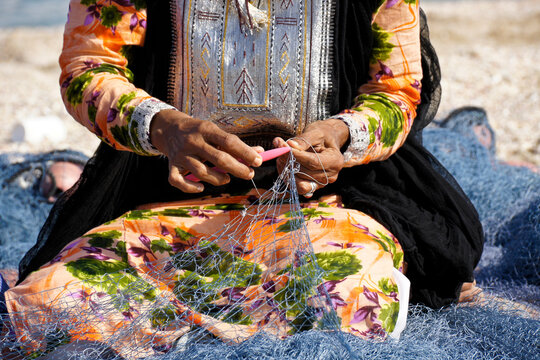 Omani woman in traditional dress mending fishing net on beach, Sur, Sultanate of Oman