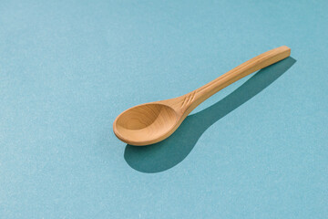 Light wooden spoon on a blue background in hard light.