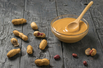 Glass bowl with peanut paste and wooden spoon on a wooden table.