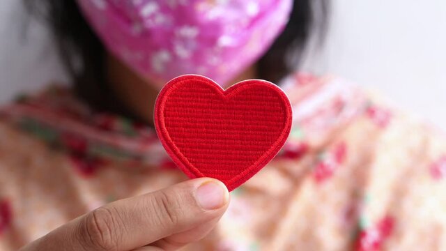 Woman in protective face mask holding heart shape 