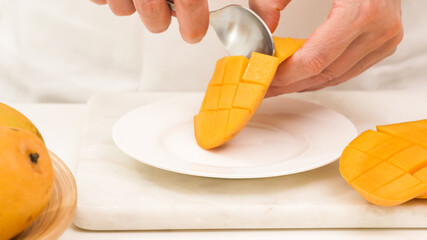 Fresh ripe organic yellow mangoes close up. Woman cutting mango on white cutting board, preparing...