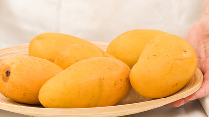 Naklejka na ściany i meble Yellow mangoes close up. Fresh ripe organic fruits on wooden plate