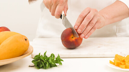 Mango, peach fruit salad. Woman cutting peach. Close up view, white background