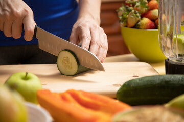 health concept, woman's hands cutting cucumber on a wooden board surrounded by fruits and vegetables