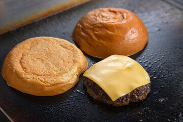 The process of preparing fast food, sandwich, hamburg. Two pieces of bun, meat cutlet and cheese for a large cheeseburger are fried on a large grill