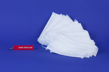 A stack of disposable medical masks and a keychain with the words remove before flight on a blue background, close-up.