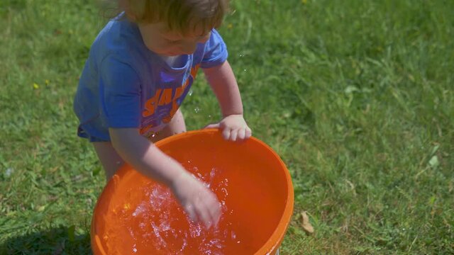 Slow motion of toddler joyfully splashing water for a bucket and getting all wet, supe fun