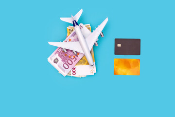 plane, a bundle of money and plastic cards on a blue background, top view with space for text. The photo symbolizes the cost of flights, earnings of airlines