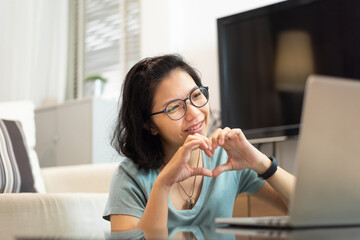 Smiling Asian woman making her hands in heart shape during video call with laptop