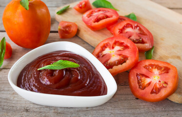 close-up bowl of ketchup or tomato sauce and fresh tomatoes on Wooden table.