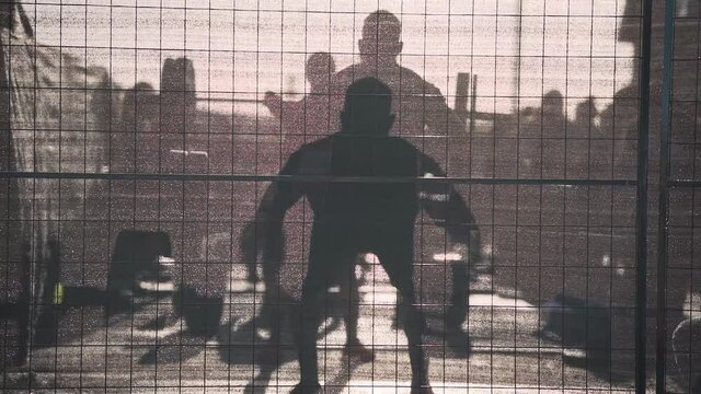 Strong man silhouette behind fence power cleaning heavy barbell during crossfit workout sunflare slow motion fitness