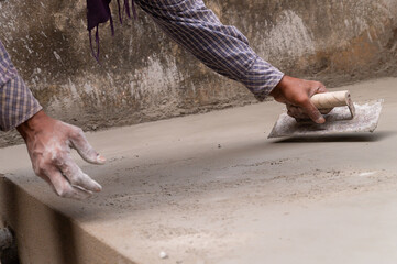 Indian labour levelling plastered floor using flat trowel and cement manually, Stock image.