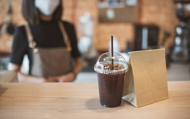Barista  in apron and face mask standing  behind counter bar ready to give Coffee Service at the modern coffee shop, Modern cafe business, Social distancing concept. 