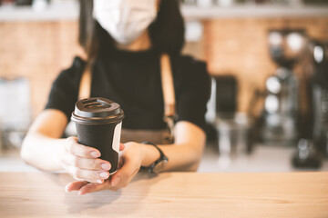 Barista  in apron and face mask standing  behind counter bar ready to give Coffee Service at the modern coffee shop, Modern cafe business, Social distancing concept. 