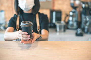 Barista  in apron and face mask standing  behind counter bar ready to give Coffee Service at the modern coffee shop, Modern cafe business, Social distancing concept. 