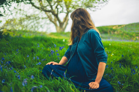 Pregnant woman in meadow of bluebells looking at tree