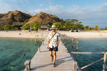 Young Asian man traveller walking on wooden bridge at Kanawa island, Flores island in Komodo national park in Indonesia. Travel and lifestyle concept