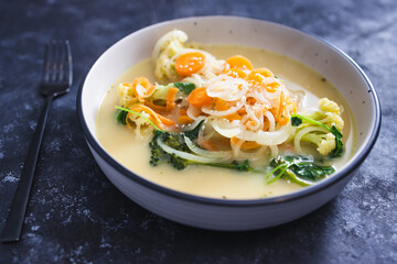 healthy plant-based food recipes concept, vegan soup with fresh veggies topping incuding caulini carrots onions and broccolini