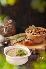 Homemade pickled honey agarics cream soup in wooden bowl and  open glass jar, spices, spoon, napkin,  on  wooden table. Marinated mushrooms. Fermented healthy food.
