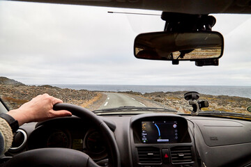 View from car window on the road and pity strange landscape with a mountains, rocks and cloudy sky and hand of woman. Landscape through windscreen in Norway